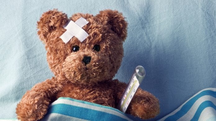 Teddy ear with plaster and thermometer on bed