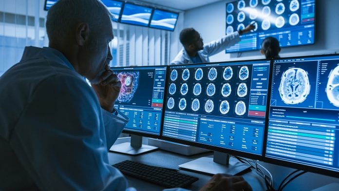Over the Shoulder Shot of Senior Medical Scientist Working with CT Brain Scan Images on a Personal Computer in Laboratory. Neurologists in Research Center Work on Brain Tumor Cure. Revolutionary investment could help diagnose breast cancer and combat diseases
