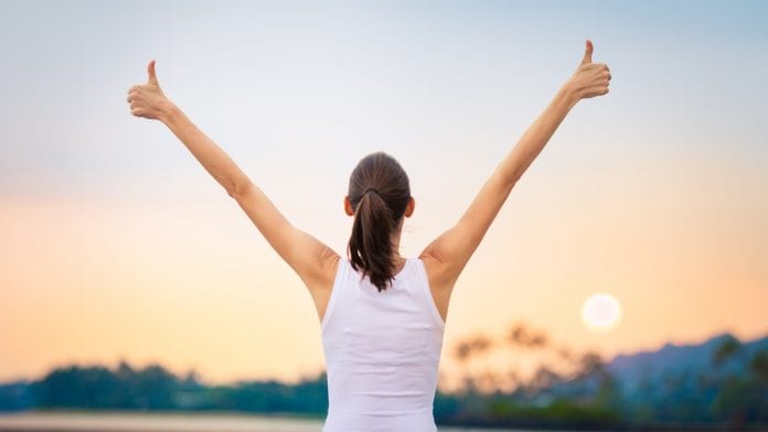 Young woman with arms in the air giving thumbs up.