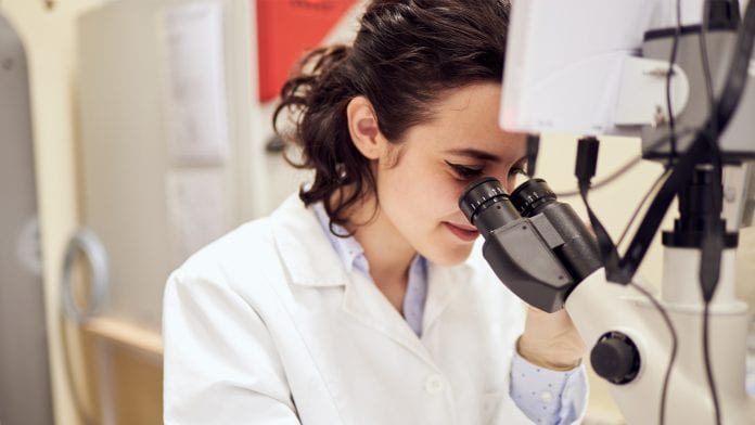 researcher in lab looking through microscope