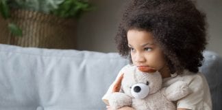Upset lonely african kid girl holding teddy bear looking away