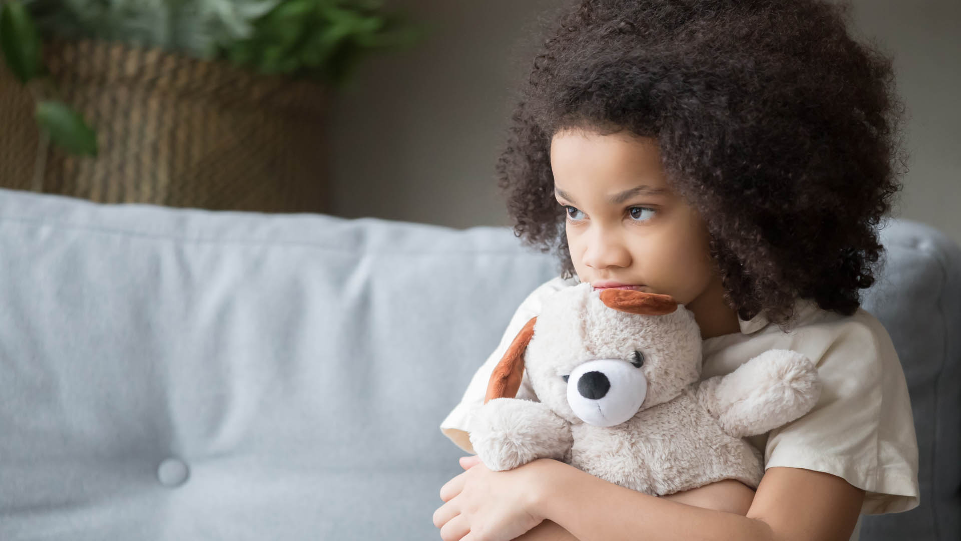 Upset lonely african kid girl holding teddy bear looking away