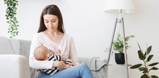 young mother breastfeeding her baby on couch