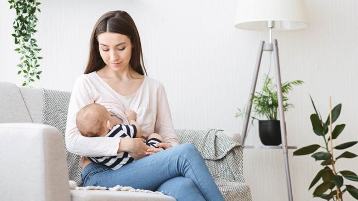 young mother breastfeeding her baby on couch