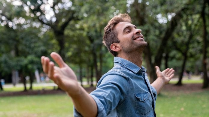 Portrait of a peaceful man relaxing at the park with arms open and smiling