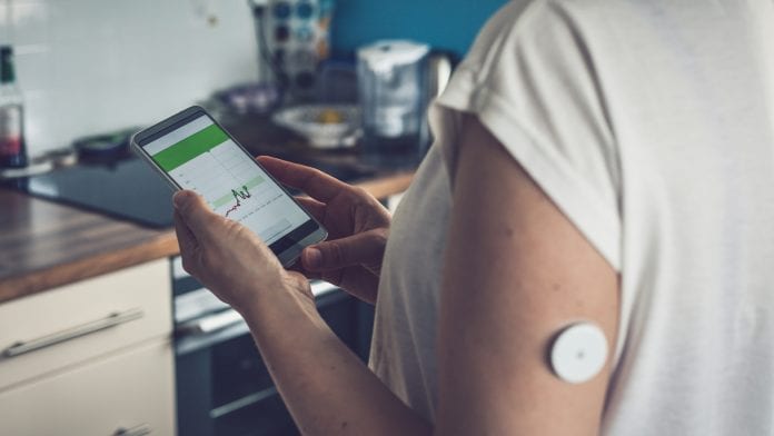 Woman checking glucose level with a remote sensor and mobile phone, sensor checkup glucose levels without blood, good result. Diabetes treatment.