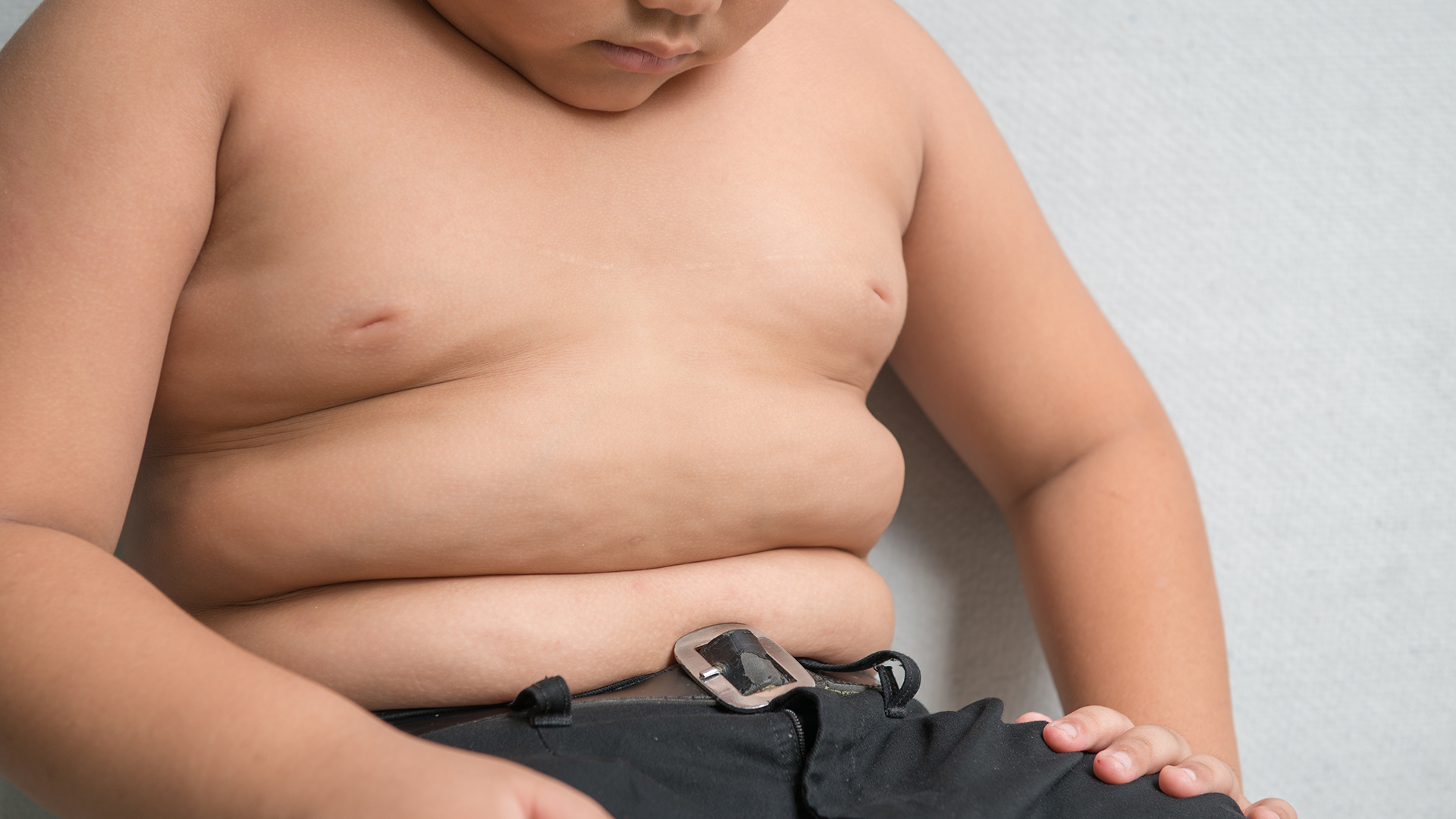 The size of stomach of children with overweight on grey background