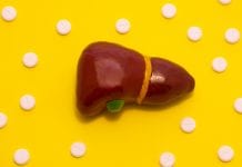 Concept photo treatment of liver diseases which are accompanied with jaundice. Anatomical liver figure lying on yellow background surrounded by white pills medicines that look like ornaments polka dot