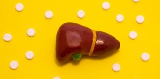 Concept photo treatment of liver diseases which are accompanied with jaundice. Anatomical liver figure lying on yellow background surrounded by white pills medicines that look like ornaments polka dot