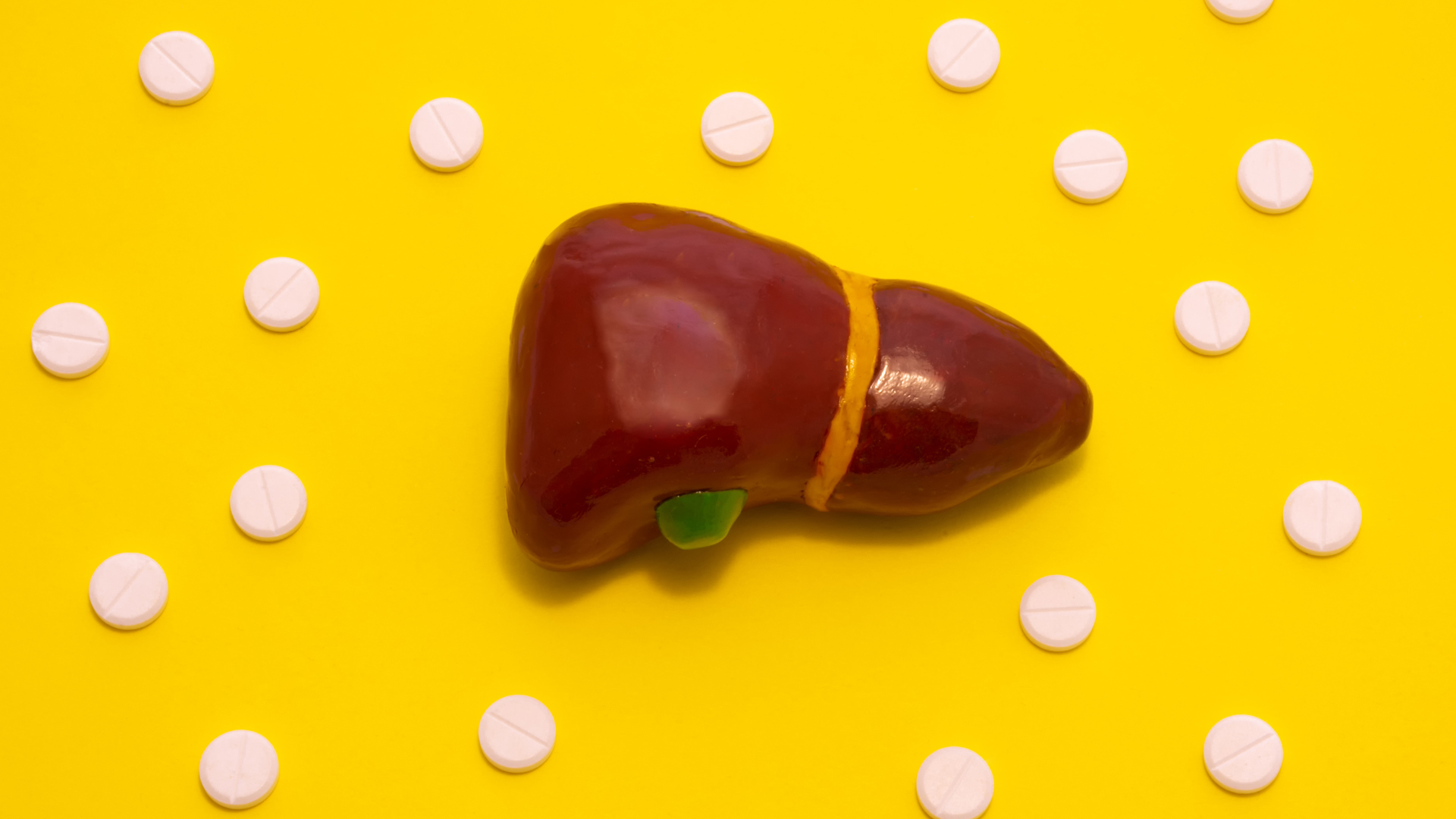 Concept photo treatment of liver diseases which are accompanied with jaundice. Anatomical liver figure lying on yellow background surrounded by white pills medicines that look like ornaments polka dot