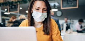 ortrait of young woman using laptop at cafe wearing face protective mask to prevent the coronavirus