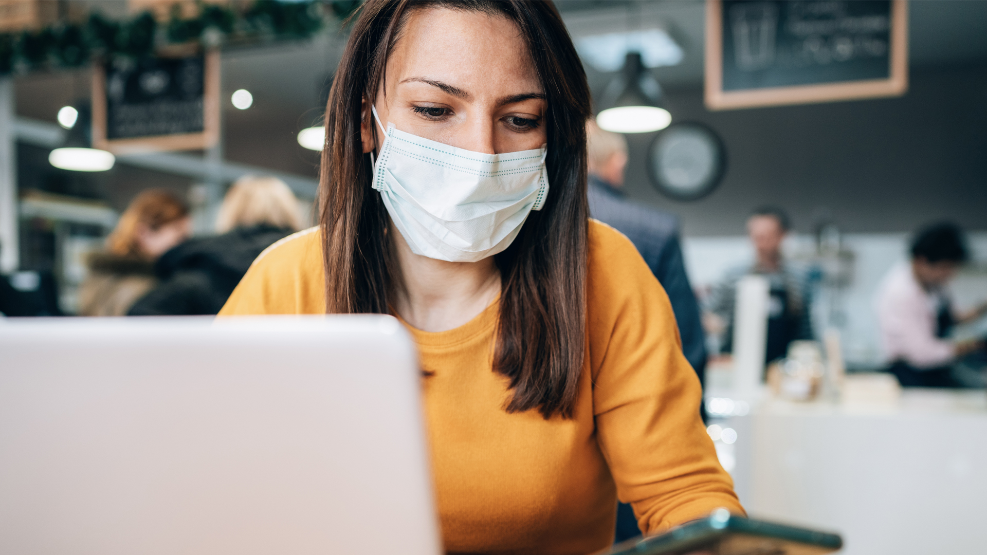 ortrait of young woman using laptop at cafe wearing face protective mask to prevent the coronavirus