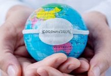 closeup of a caucasian doctor man holding a world globe with a protective mask with the word coronavirus written in it