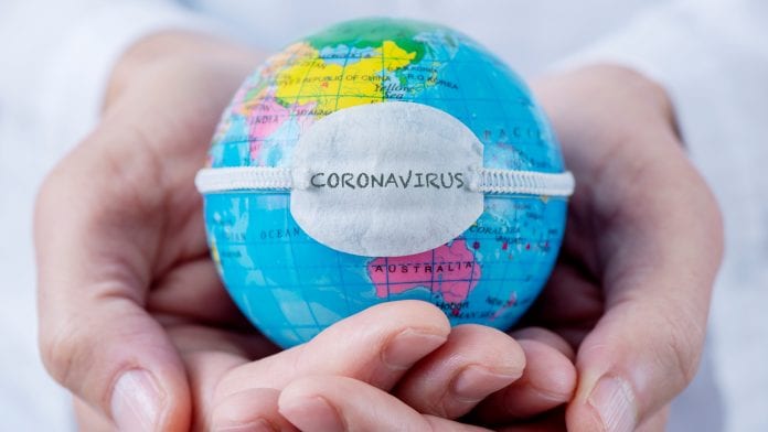 closeup of a caucasian doctor man holding a world globe with a protective mask with the word coronavirus written in it