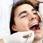 Young man having medical procedure at dentist office. Dentist drilling and cleaning teeth.