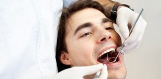Young man having medical procedure at dentist office. Dentist drilling and cleaning teeth.