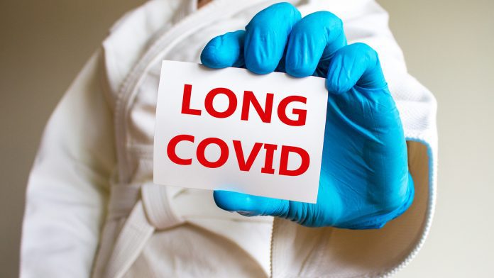 COVID-19 long covid symbol. A young strong man in a white kimono for sambo, jiu jitsu and other martial arts with a blue medical gloves. White card with words 'long covid'. Long covid concept. long COVID treatment
