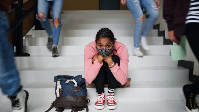 Depressed young student with face mask sitting on floor back at college or university, coronavirus concept. mental health support