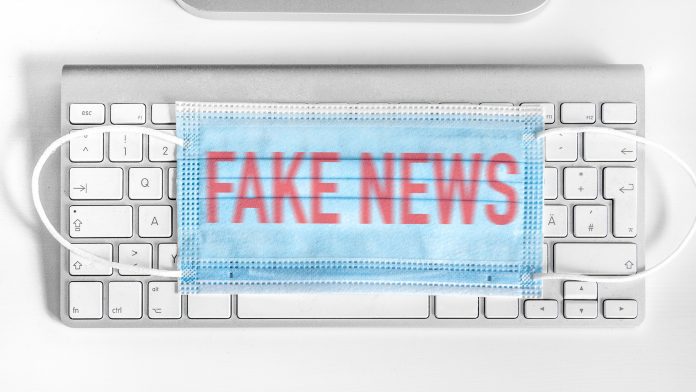 Corona respirator lying on the computer keyboard. Red inscription - FAKE NEWS vaccine hesitancy