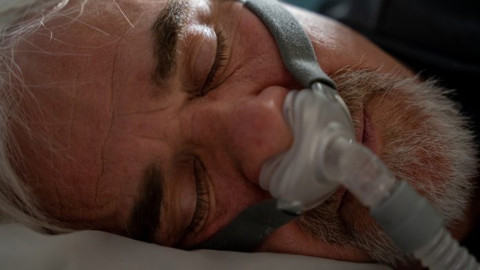 Mature Man Sleeping with a CPAP (Continuous positive airway pressure) Machine after being diagnosed with Sleep Apnea CPAP machines