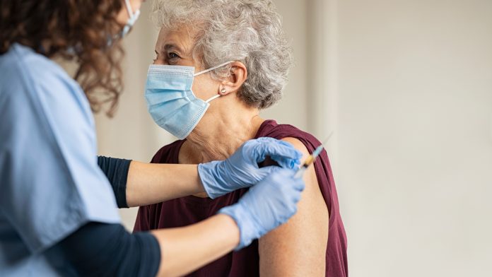 Doctor giving Covid vaccine to senior woman NHS Covid booster