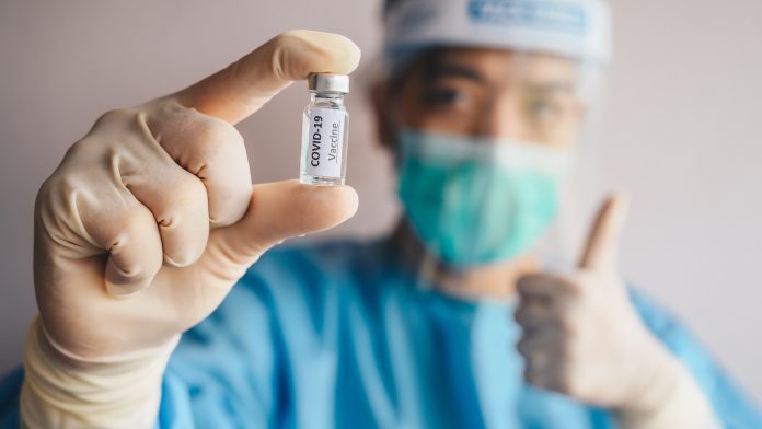 Scientist doctor holding a sample test bottle of Covid-19 vaccine and showing thumb up. vaccine safety