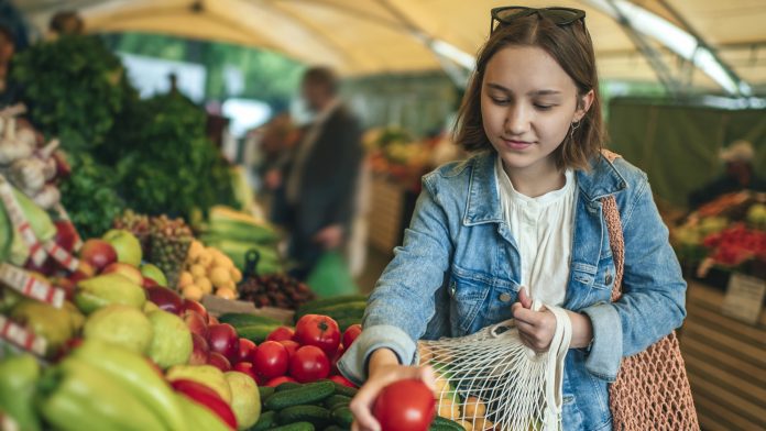 Young girl choosing vegetables and fruit at a farmers market with reusable bag, plastic free and zero waste concept planetary health diet